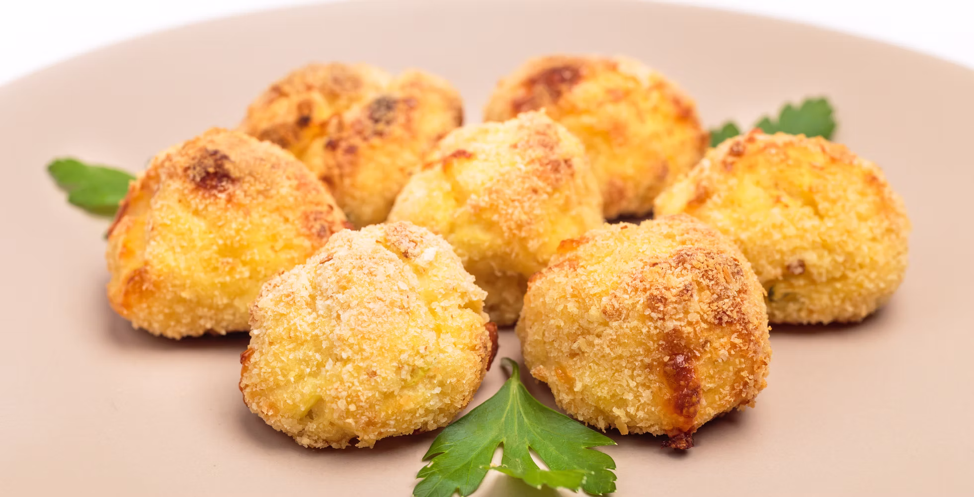 Polpette di zucchine e patate al forno, dorate, su un piatto beige con foglie di prezzemolo