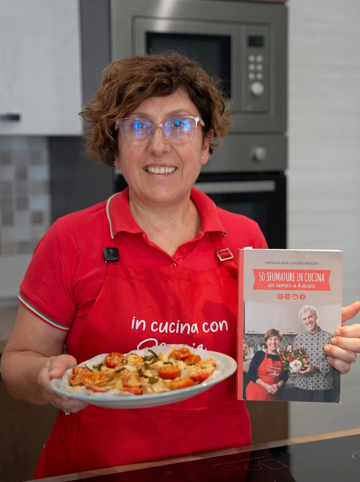 Nuccia Alboni in cucina con il libro in una mano e un piatto nell'altra