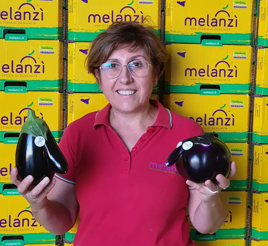Nuccia Alboni con due melanzane in mano davanti alle cassette Melanzì