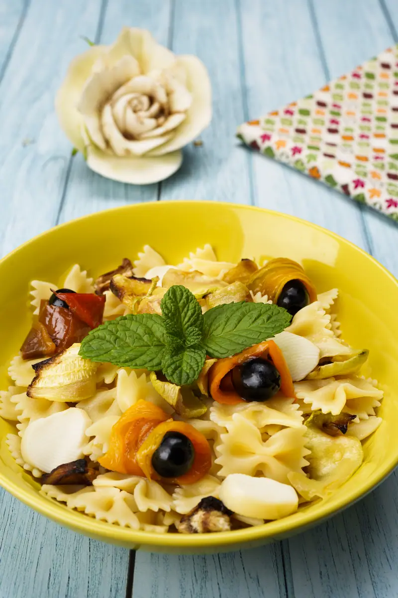 Farfalle con melanzane e peperoni grigliati, olive nere, formaggio e menta, in una ciotola gialla