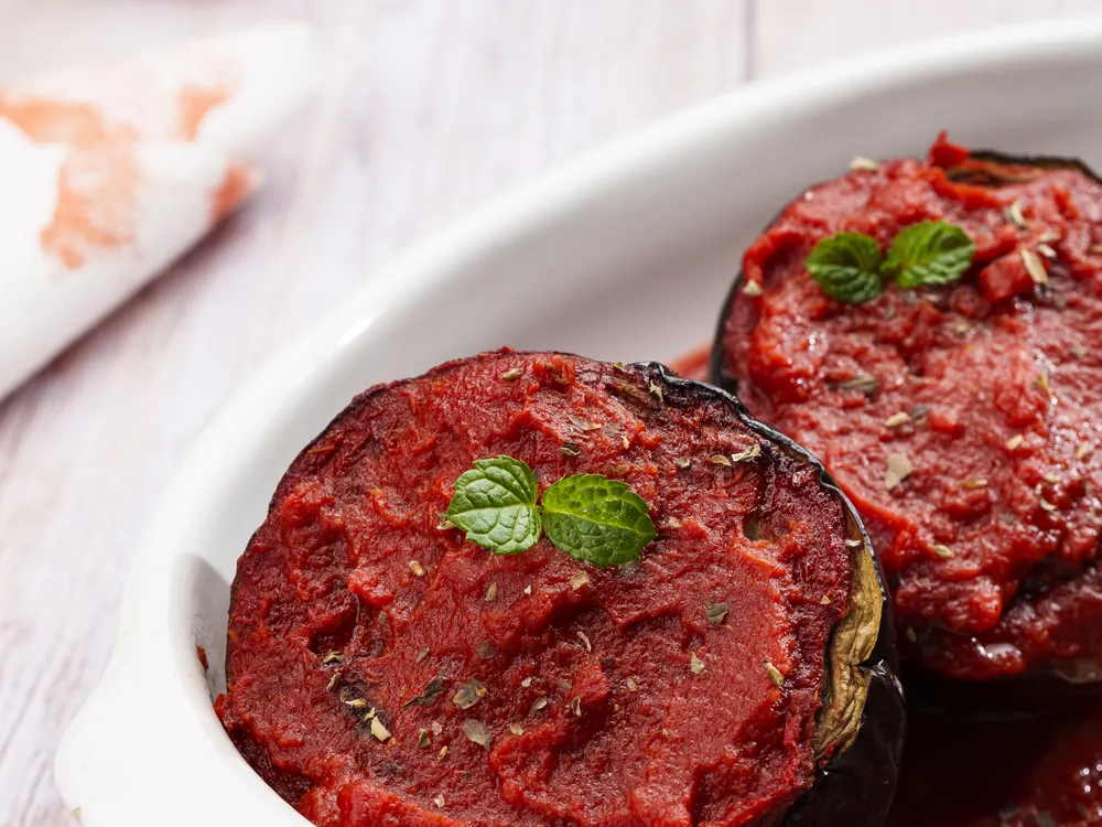 Melanzane 'mbuttunate con salsa di pomodoro e foglioline di menta, in una teglia ovale bianca