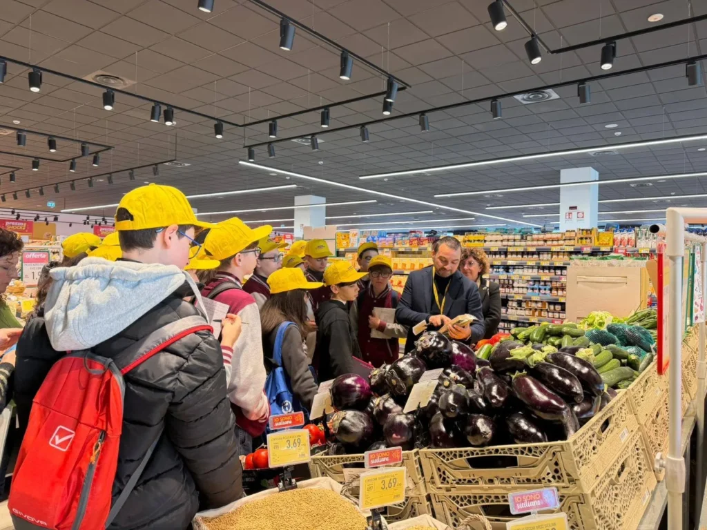 Bambini con il cappellino giallo davanti alle cassette di melanzane nel reparto ortofrutta