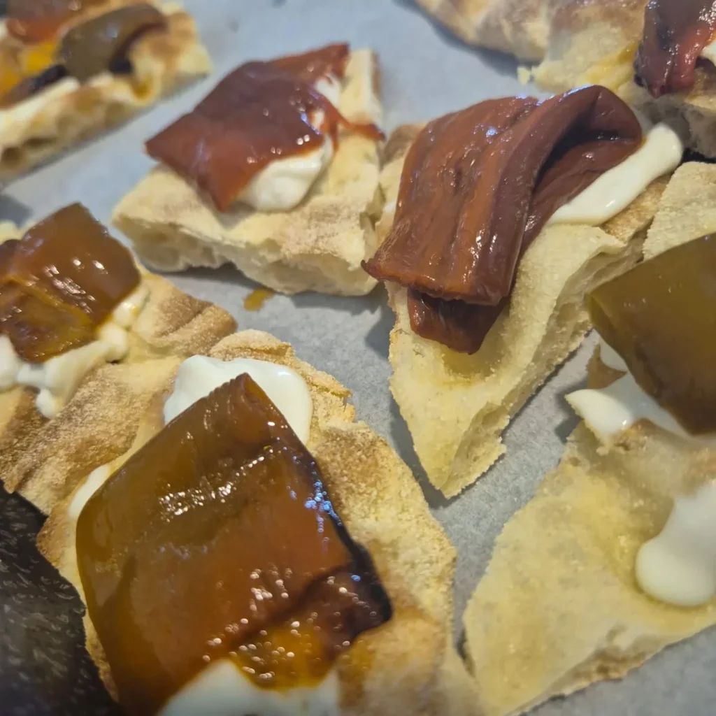 Fette di pinsa condite con ortaggi cotti e crema bianca, servite come assaggio