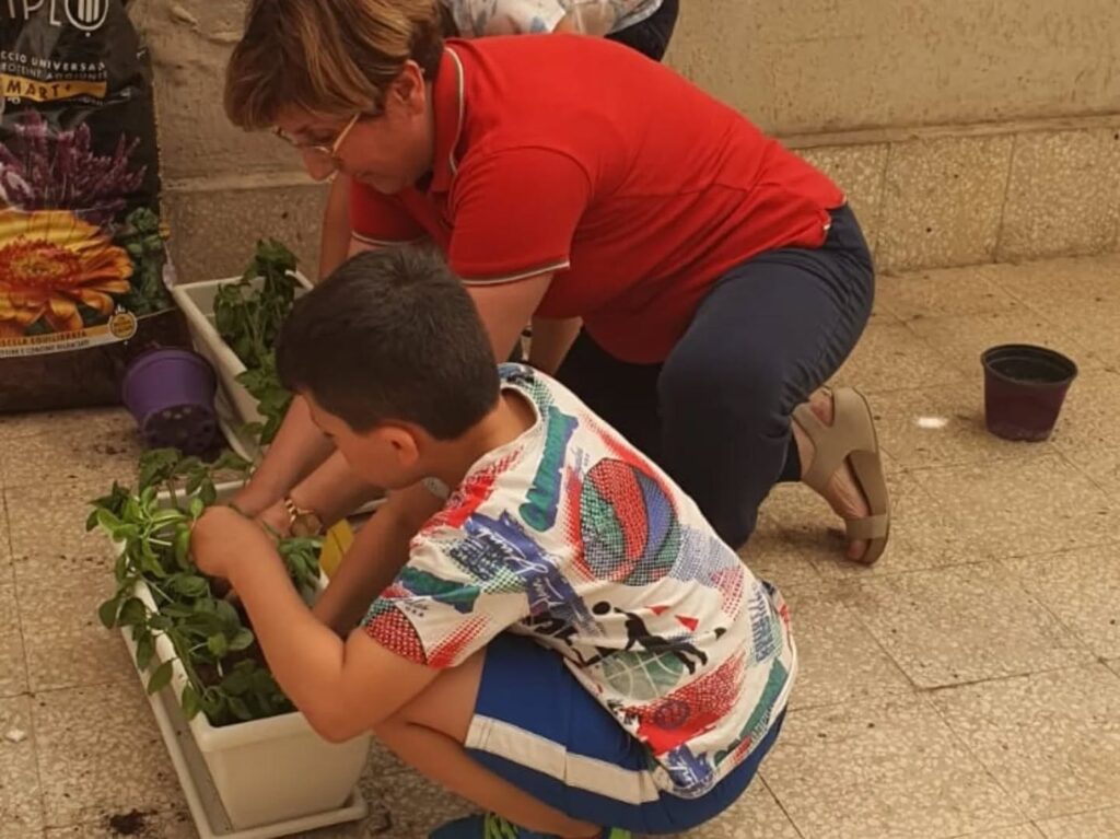 Nuccia Alboni aiuta un bambino a trapiantare una piantina in vaso